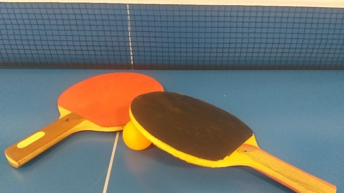 Zwei Tischtennisschläger mit kontrastierenden orange-schwarzen Belägen, die auf einem blauen Tisch liegen.