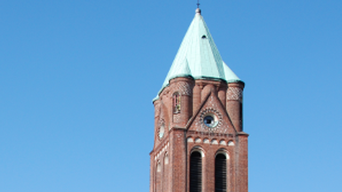 Große rote Backsteinkirche mit hohem Turm und spitzem Dach.