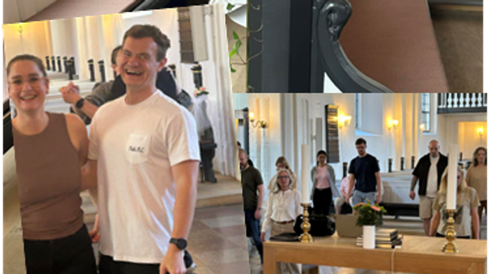 Et glædesfyldt par poser i en pyntet kirke med blomsterdekorationer og en festlig forsamling i baggrunden.