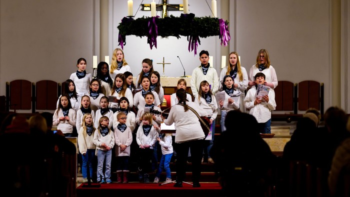 Ein Kinderchor tritt in einer Kirche auf, gekleidet in abgestimmte weiße Kleidung mit einem geschmückten Altar im Hintergrund.