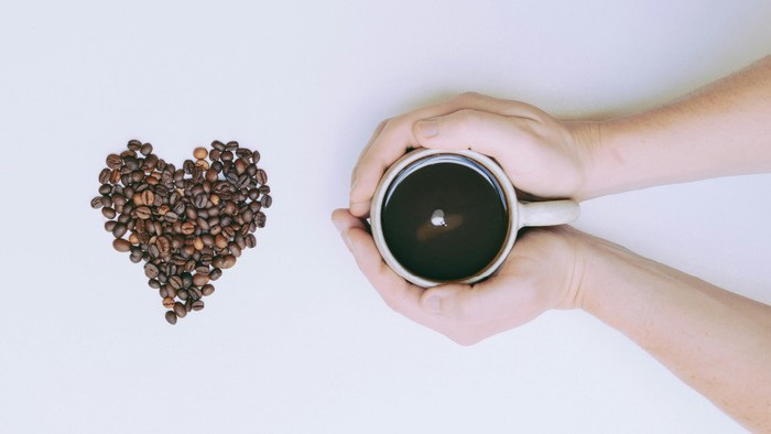 En hånd holder en kaffekop ved en hjerteformet kaffebønneanordning og en skøn.