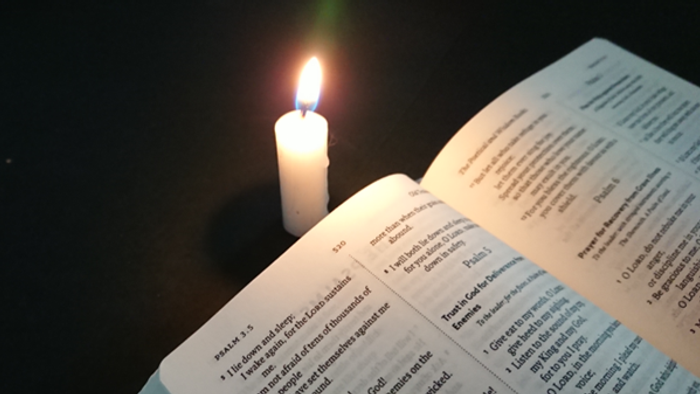 Candle burning next to open book with text.