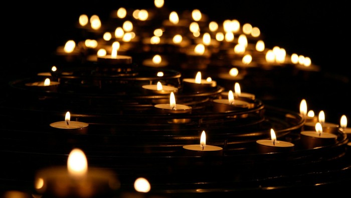 A dense arrangement of lit candles glowing warmly against a dark background.