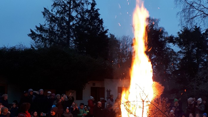 Eine Gruppe von Menschen um ein großes Lagerfeuer im Freien bei Dämmerung.