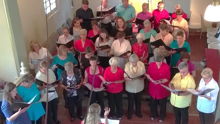 Eine vielfältige Gruppe von Sängerinnen und Sängern singt harmonisch in einer Kirche, geleitet von einem Dirigenten.
