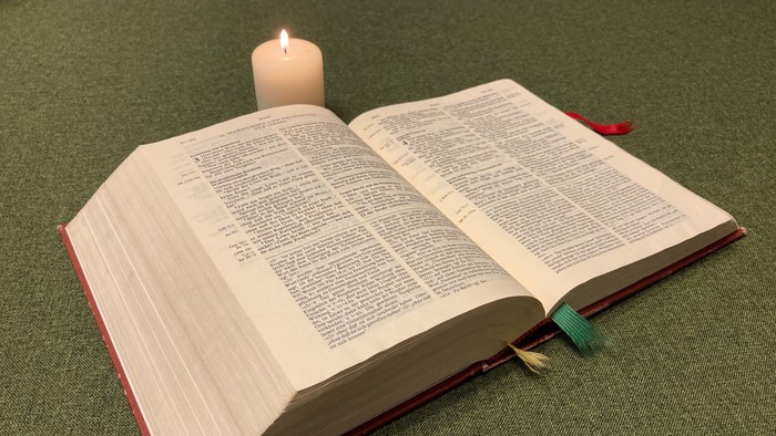 Offenes Buch mit brennender Kerze darauf auf grüner Oberfläche