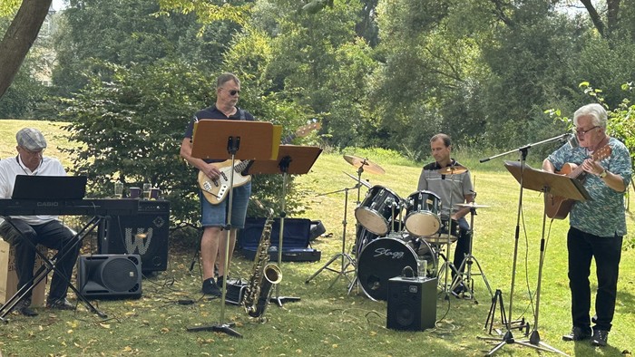 Eine Musikergruppe im grünen mit Keybord, Bass, Schlagzeug, Gitarre und Saxophon