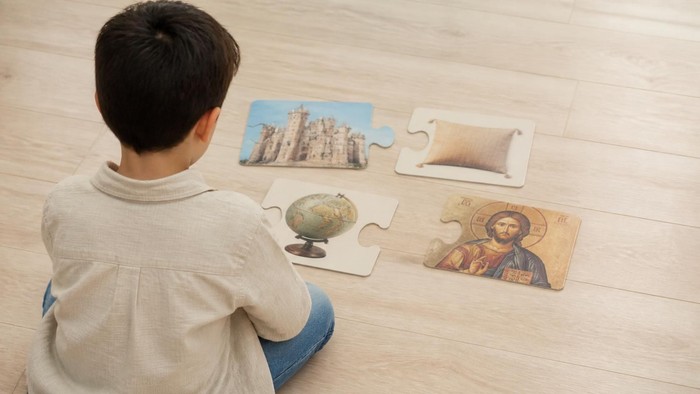 Ein Kind sitzt auf dem Boden und setzt lehrreiche Puzzleteile mit einem Globus und einem religiösen Symbol zusammen.