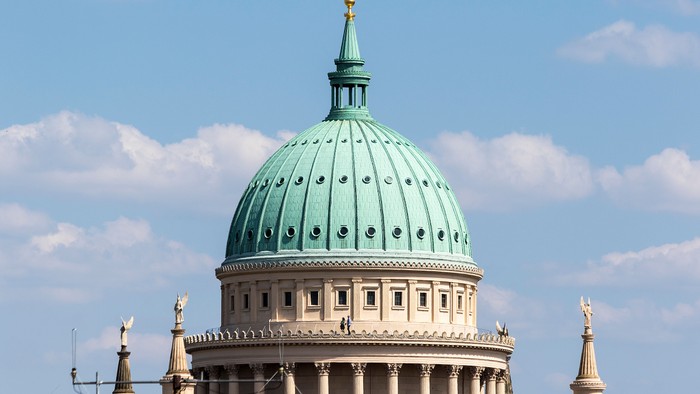 Das Bild zeigt eine Kuppelkirche mit grüner Kuppel und goldenen Akzenten vor blauem Himmel.