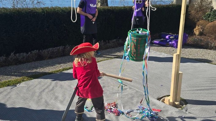 Børn leger med en hjemmelavet gynge lavet af stof og reb på en sandet overflade udendørs.