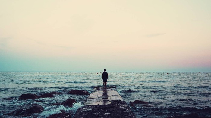 Eine einsame Gestalt steht nachdenklich auf einem Pier in der Abenddämmerung am Meer.