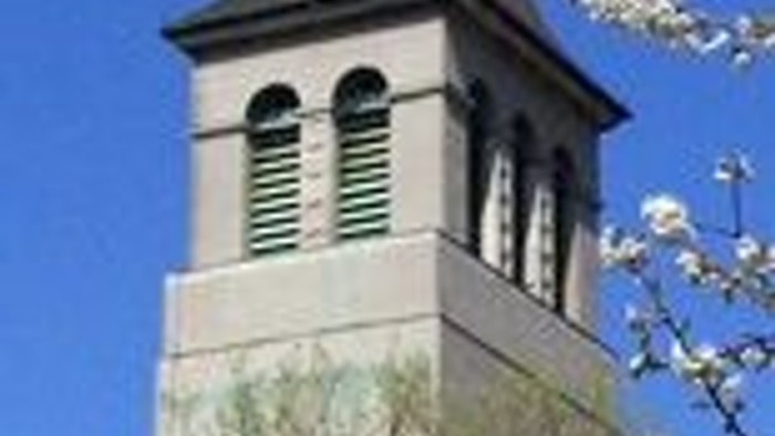 Ein hoher Turm mit Uhr und spitzem Dach vor blauem Himmel.