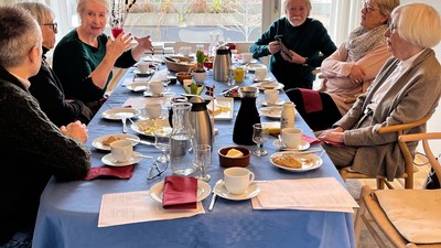 En gruppe mennesker, der nyder en social te-sammenkomst omkring et langt bord med forskellige snacks og drikkevarer.