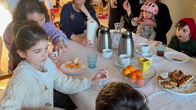 Familien samles omkring et bord og nyder et måltid med forskellige retter og drikkevarer.