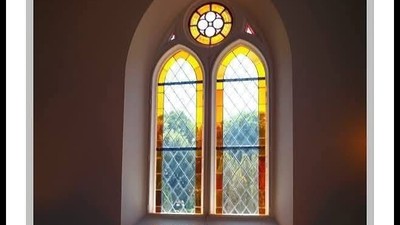 Farvet glasvindue oplyser træbænkene i det fredfyldte kirkeinteriør under solnedgang.