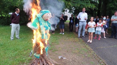 En farverig figur bliver brændt i et ceremonielt bål, mens tilskuere ser på.