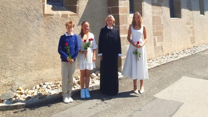 Fire personer med blomster poserer uden for en historisk stenkirke på en solskinsdag.