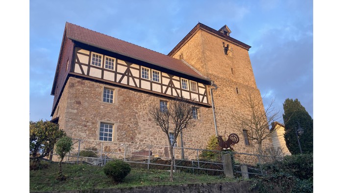 Altes Steinschloss mit Fachwerk, umgeben von Bäumen und Himmel.
