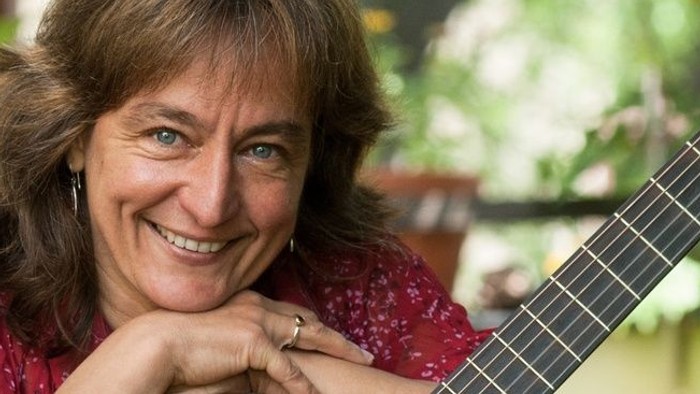 Eine Frau mit Gitarre lächelt in die Kamera.