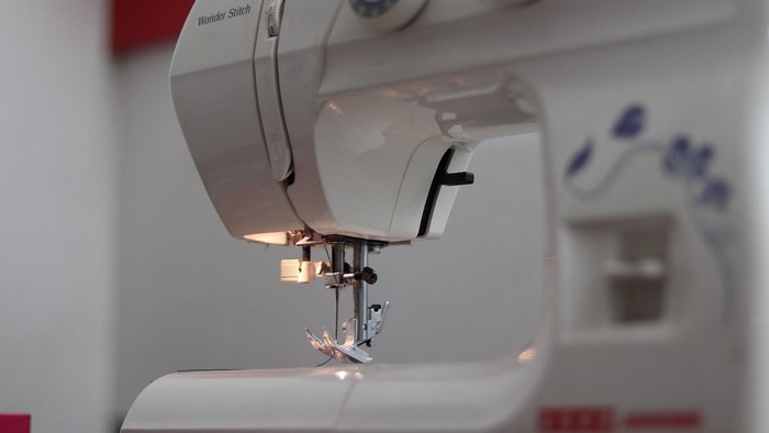 Nahaufnahme einer Nähmaschinennadel, die über dem Stoff schwebt, bereit zum Nähen.