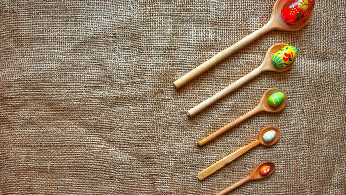 Bunte Holzlöffel mit aufwendigen Malereien auf einem Jutestoff-Hintergrund.