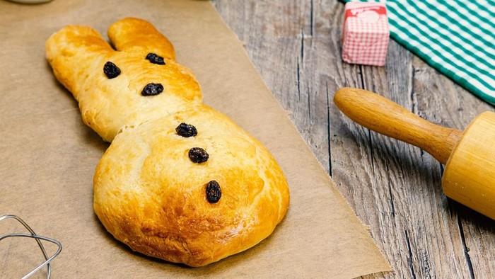 Goldenes Gebäckbrötchen in Hasenform mit Rosinenaugen auf Backpapier.