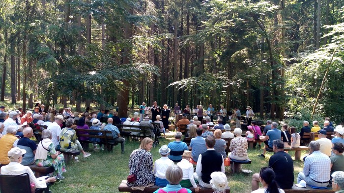 Im Wald versammelte Menschen auf Picknickdecken, umgeben von Bäumen.