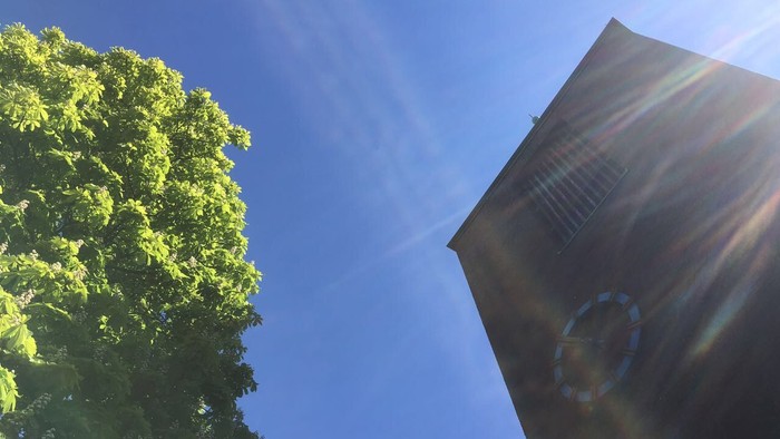 Der Kirchturm vor dem Maihimmel mit Kastanienbaum in voller Blüte.