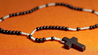 Ein schwarzes Kreuz hängt an einer Perlenkette auf einem orangen Hintergrund