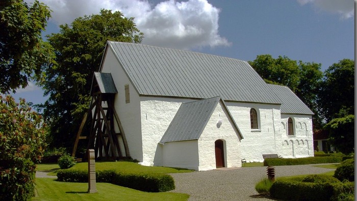 Et hvidt kirkebygning med trætårn og græsplæne foran