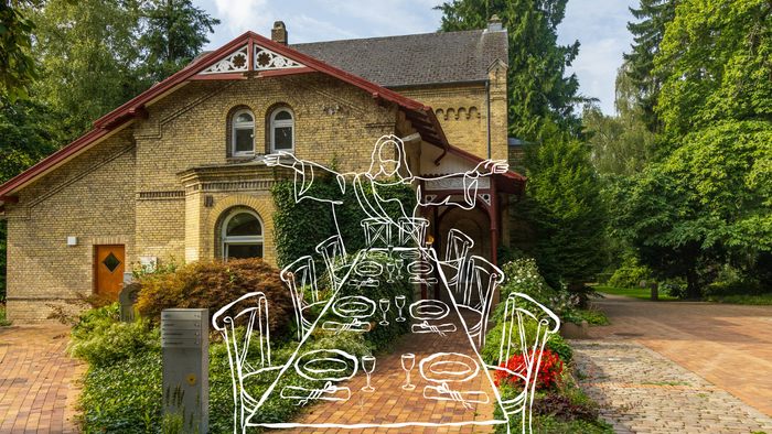 Ein skurriles Metallskulptur steht vor einem charmanten Haus mit rotem Dach und umgeben von üppigem Grün.