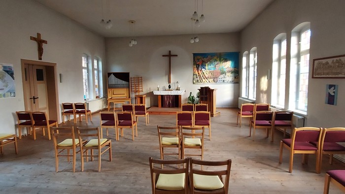Geräumige Kapelle mit hölzernen Stühlen als Sitzgelegenheit, ausgestattet mit religiöser Kunst und einem zentralen Altarraum.