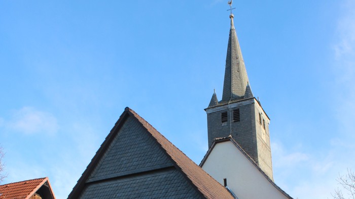 Außenansicht der evangelischen Kirche in Viesebeck. Weiß verputztes Kirchenschiff mit dunklem Dach und Turm mit schieferverkleideter Spitze.