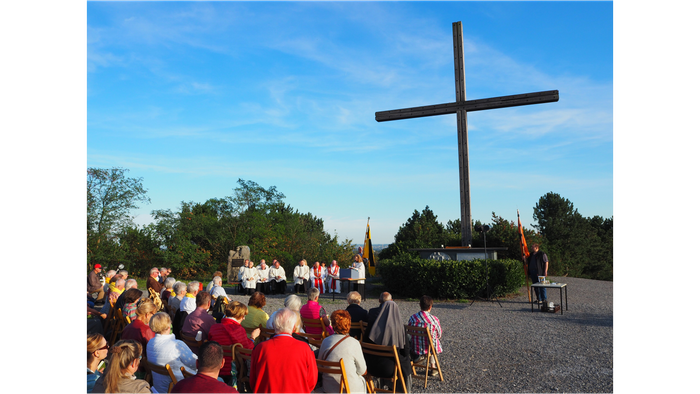 Eine Menschenmenge versammelt sich vor einem großen Holzkreuz im Freien.