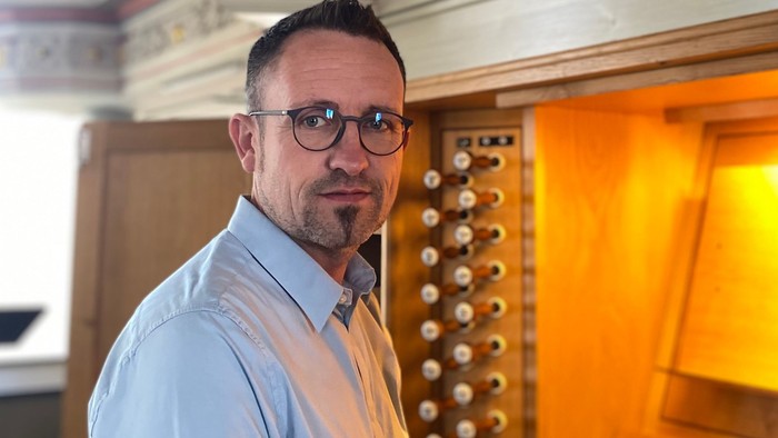 Mann mit Brille, der in der Nähe der Orgel steht.