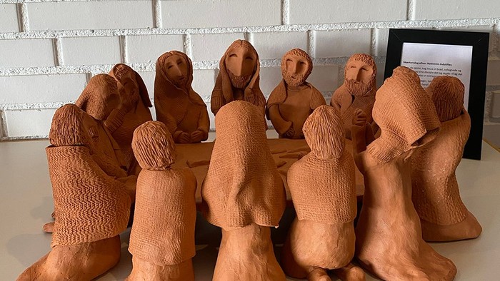 En række lille keramiske figurer af mennesker sidder på en hvid flisevæg