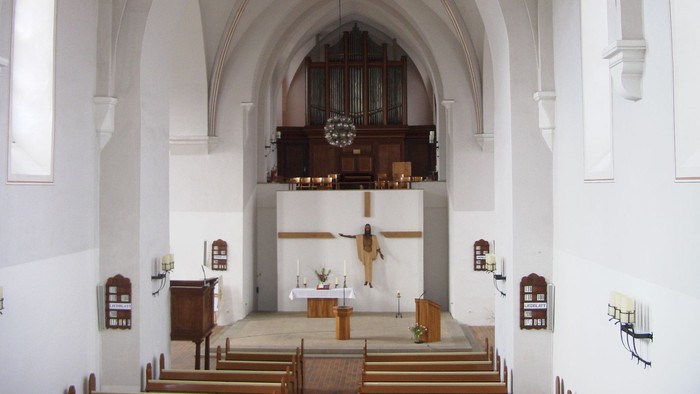 Elegante Kircheninnenausstattung mit Altar, Orgel und hölzernen Kirchenbänken unter gewölbten weißen Wänden.
