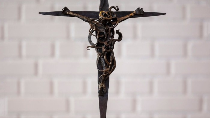 En smedejernskulptur af Jesus Kristus på korset står på en hvid flise.