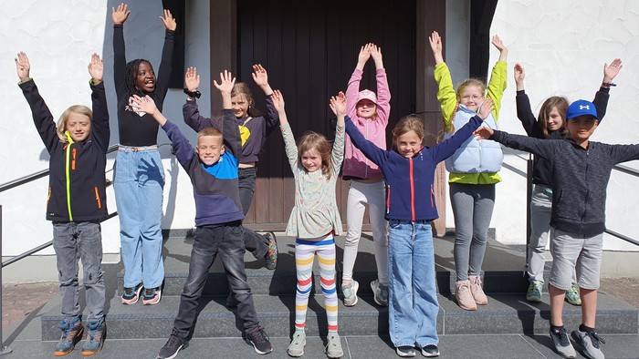 Eine Gruppe von Kindern posiert fröhlich mit erhobenen Armen auf den Stufen vor einem Gebäudeeingang.