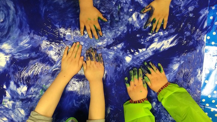 Kinder zeigen ihre bunt bemalten Hände auf blauem Hintergrund