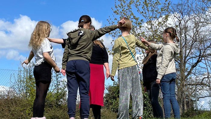 En gruppe af unge står sammen i en park og kigger op i træerne.