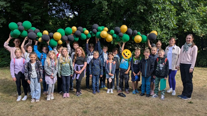 Gruppe von Kindern, die bunte Luftballons in einem fröhlichen Outdoor-Foto mit einem Erwachsenen halten.