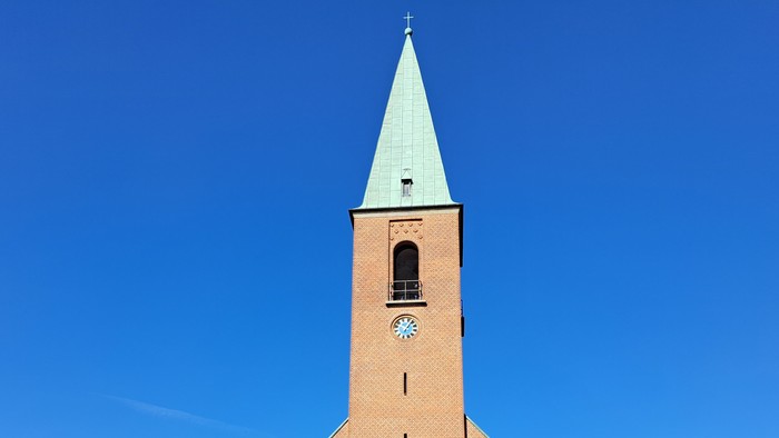 En murstenskirke med et højt spir og nationalflag, sat mod en klar blå himmel.