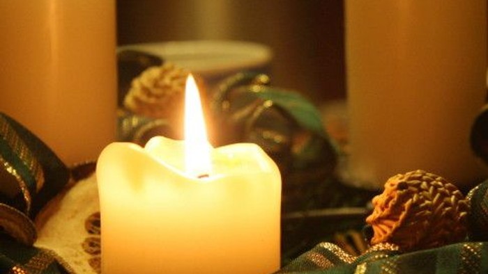 Drei Kerzen, eine angezündet, auf grünem Hintergrund