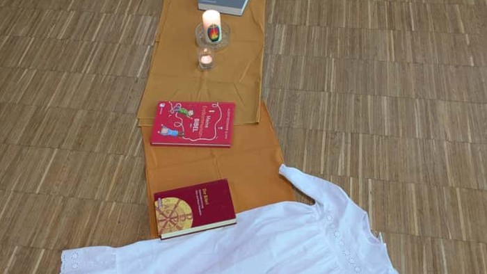 Religiöser Altaraufbau mit Büchern, Kerzen und einem weißen Tuch auf einem Holzboden.