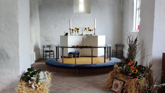 Kapel med alter, blomsterarrangeringer og hængende lys.