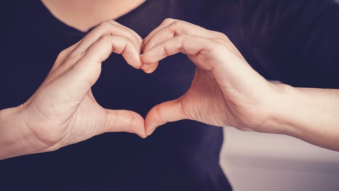 Zwei Personen halten sich an den Händen und formen ein Herz.