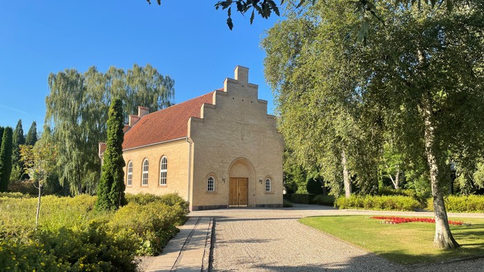 En lille kirke med rødt tag og træer i en park.
