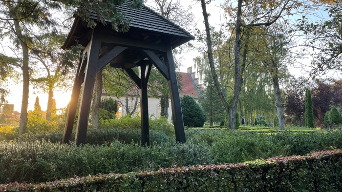 En lille træbygning i en have med buske og træer