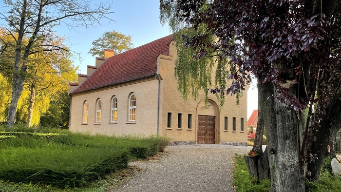 En smuk kirke med rødt tag og hvide vinduer, omgivet af grønne træer og en gravedej.